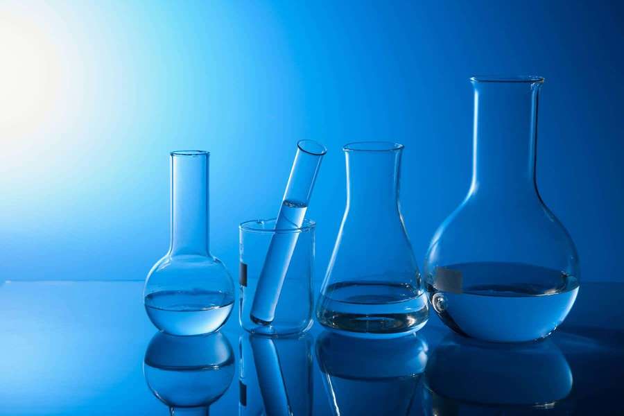 Scientific glassware with clear liquid on reflective surface under blue light. — Laboratory Wallpaper