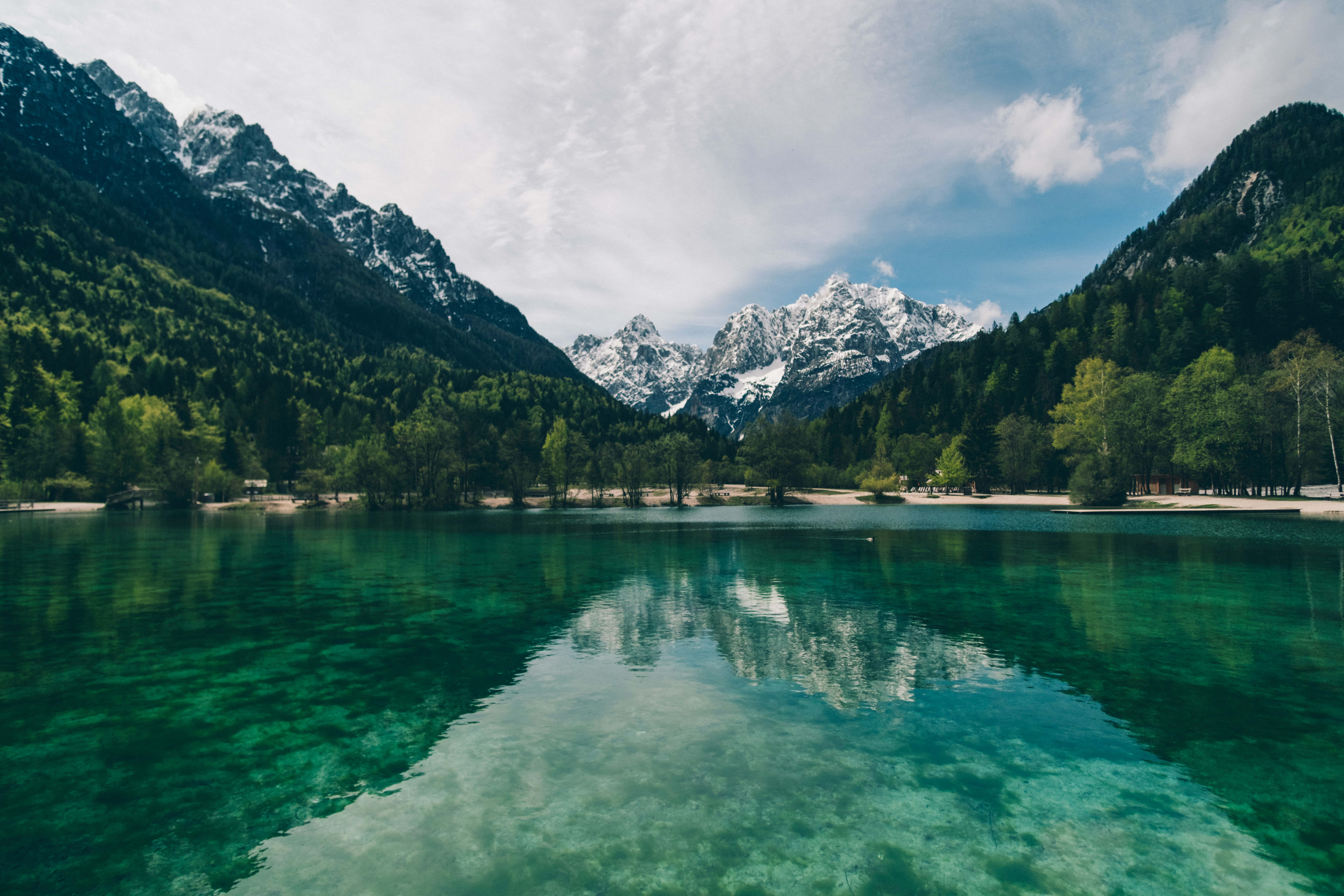 Klar turkis sø omgivet af skovklædte bjerge med sneklædte tinder reflekteret i roligt vand. — Lake Wallpapers