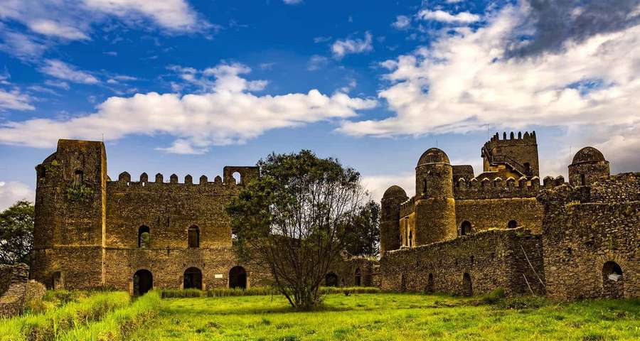 Ancient stone fortress with domed towers and crenellated walls under a bright blue sky. — Lalibela Wallpaper
