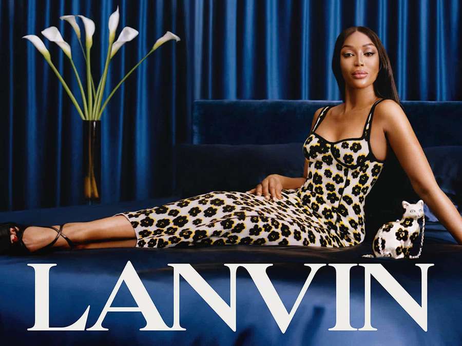 A woman in a floral dress lounges on a blue couch with calla lilies and a cat figurine beside her. — Lanvin Wallpaper