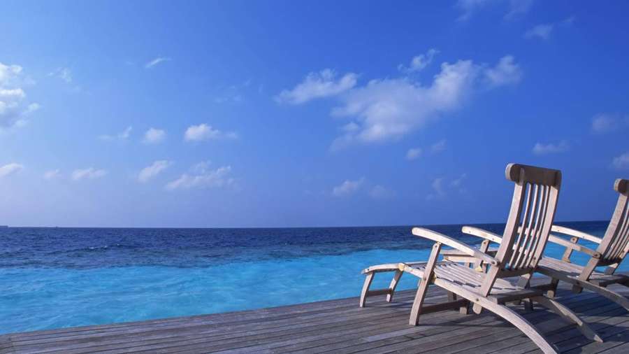 Zwei Holzliegestühle auf einer Holzterrasse mit Blick auf das türkisfarbene Meer und den blauen Himmel. — Laptop Desktop Wallpaper