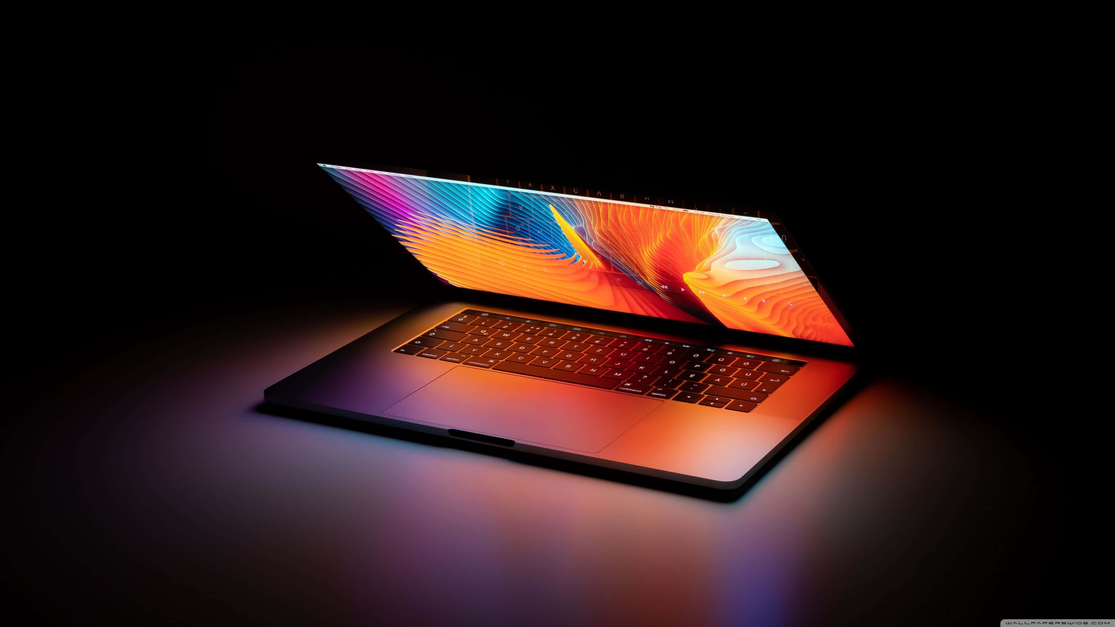 Slank bærbar computer med levende abstrakt skærm, der lyser i mørke omgivelser — Laptop Wallpapers
