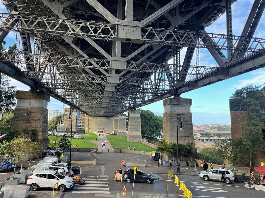 Vista desde debajo de un gran puente de acero que muestra coches y peatones en un parque urbano. — Las Rocas Sídney Fondos de pantalla