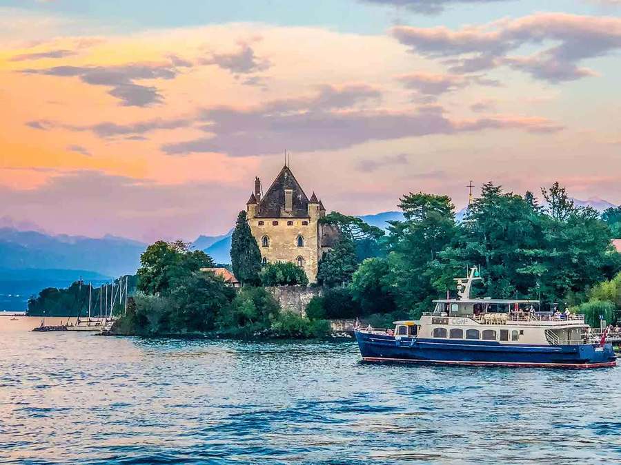 Castle on island with boat passing by at sunset — Lausanne Wallpaper