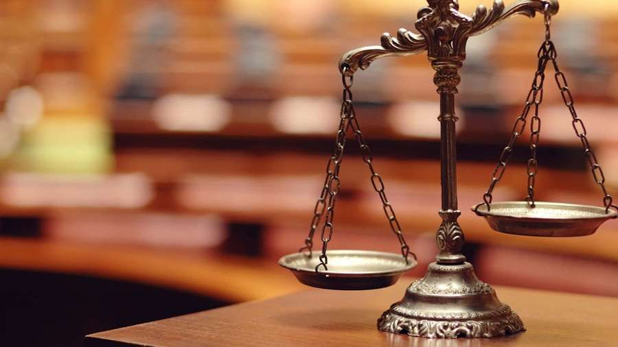 A justice scale on a wooden table in a courtroom setting. — Lawyer Background