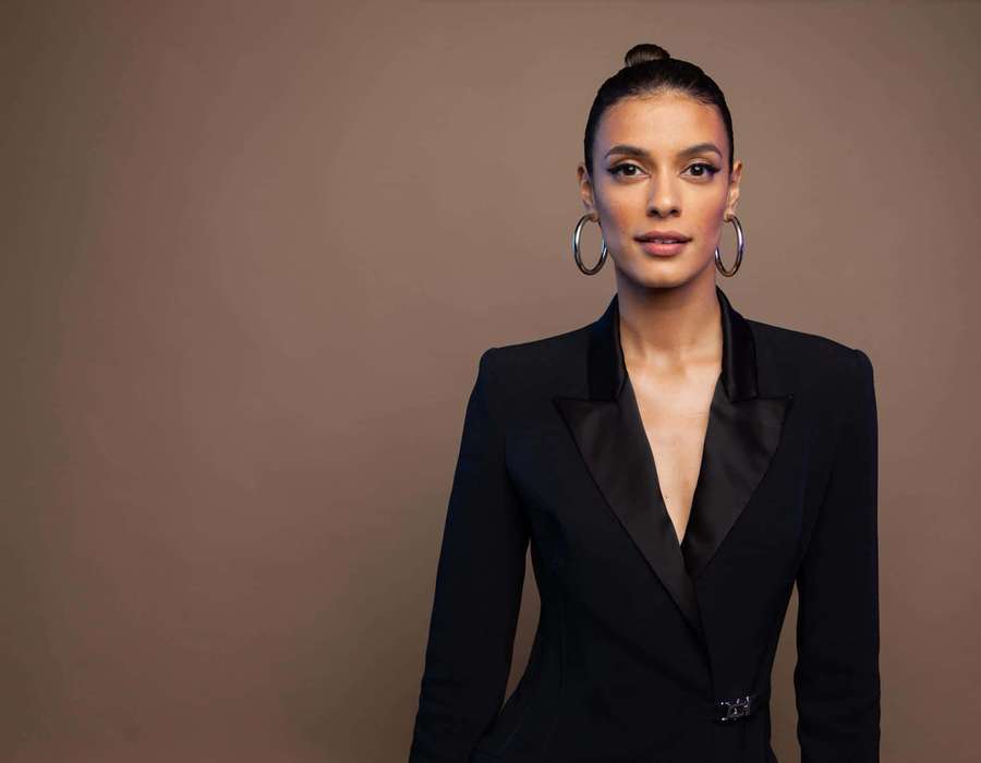 Uma mulher em um blazer preto com brincos posa contra um fundo marrom. — Laysla De Oliveira Papéis de Parede