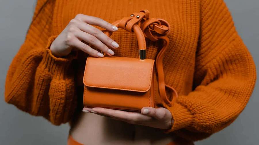 Person, die eine orangefarbene Handtasche hält, die zu ihrem Pullover in einem Studio-Setting passt. — Leder Hintergrund Hintergrundbild