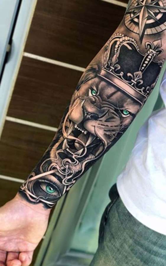 El antebrazo tatuado de una persona con un león coronado de ojos verdes y un símbolo de ojo. — León Fondos de pantalla