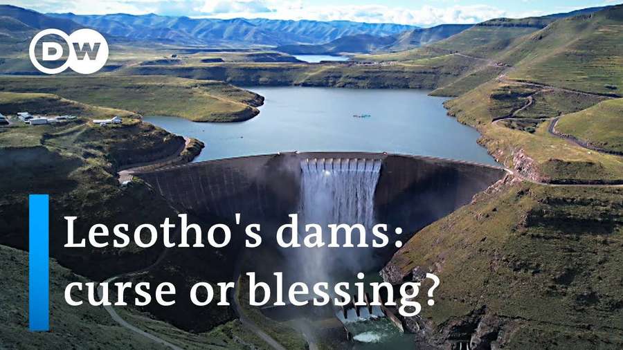 A large dam releases water into a valley with green hills and mountains in the background. — Lesotho Wallpaper