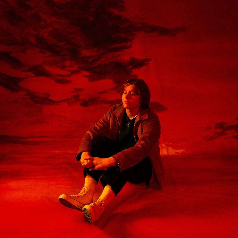 A person sits alone in a surreal red landscape under a stormy sky. — Lewis Capaldi Wallpaper