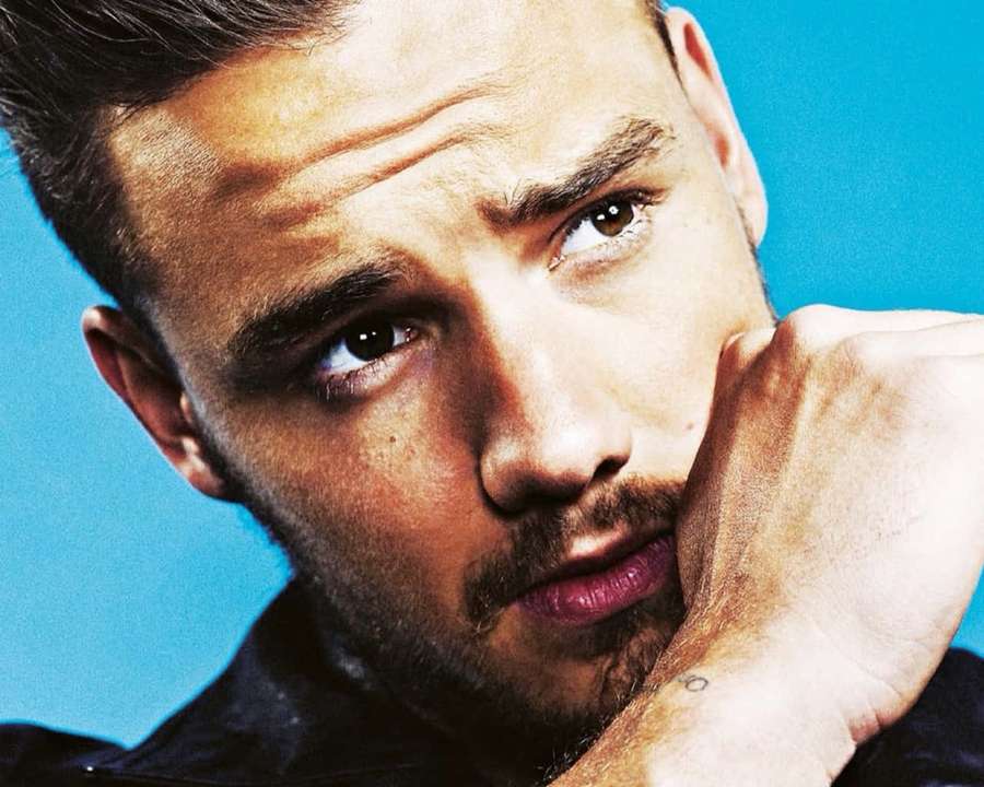 Close-up portrait of a man with intense gaze and stubble against blue background. — Liam payne Wallpaper