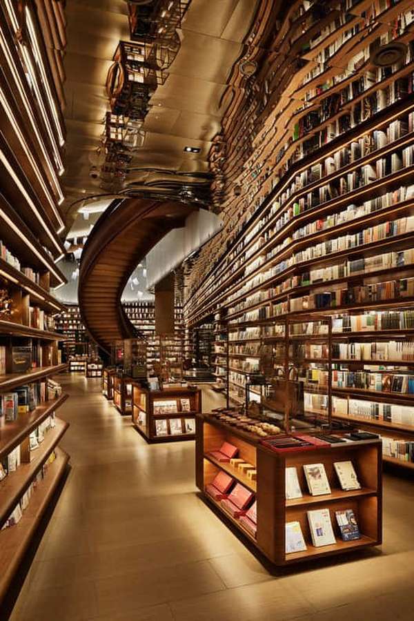 Grand library with curved bookshelves and spiral staircase under warm lighting. — Library Picture