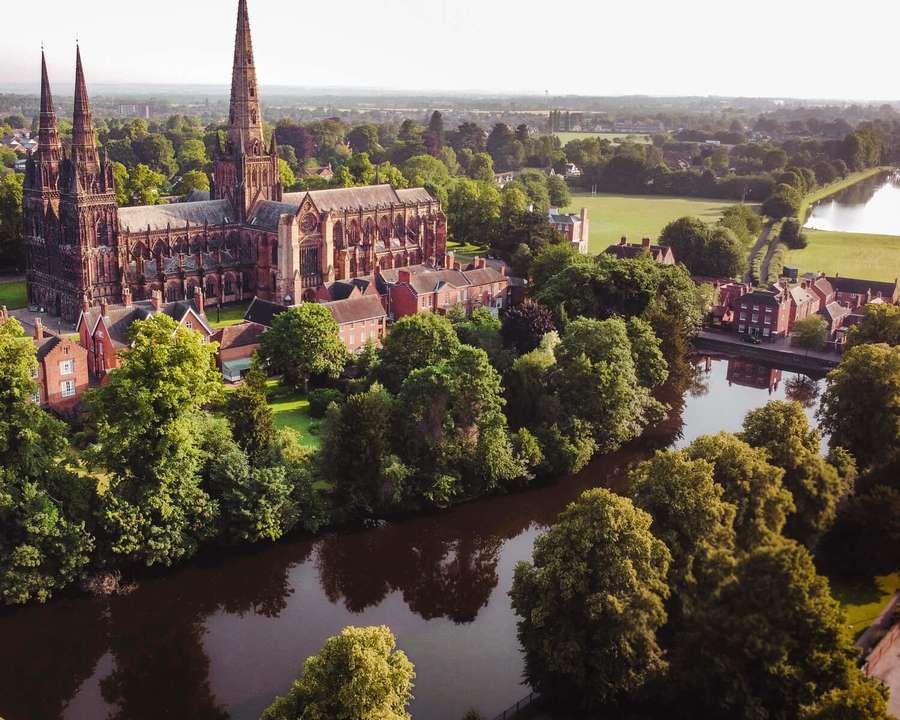 Aerial view of a historic cathedral surrounded by trees and a river. — Lichfield Wallpaper