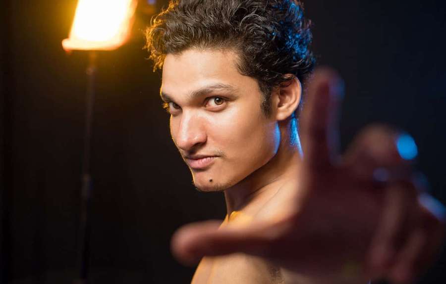 Ein hemdloser Mann mit lockigem Haar starrt intensiv, während er in einem Studio die Hand nach vorne streckt. — Light Skin Boy Wallpaper