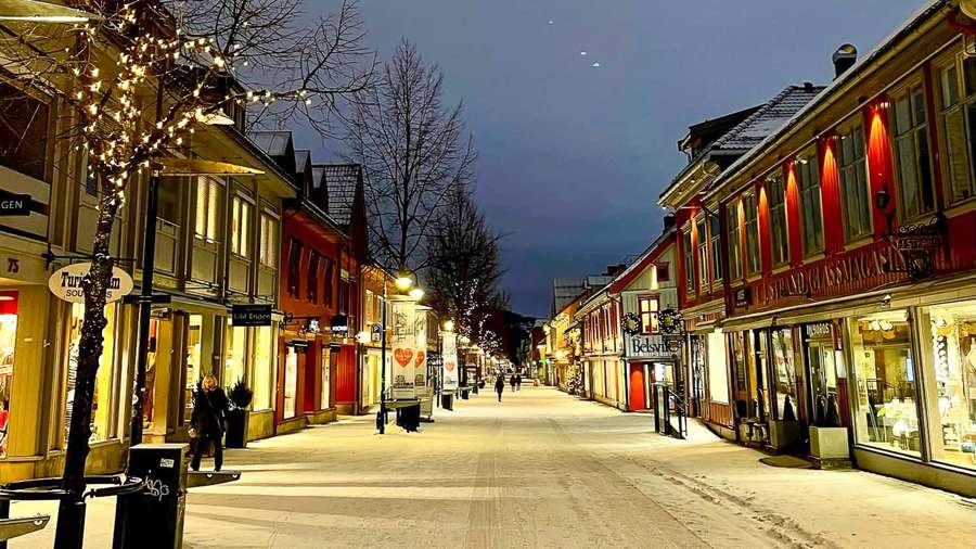 Snowy street lined with lit shops and bare trees at dusk. — Lillehammer Wallpaper