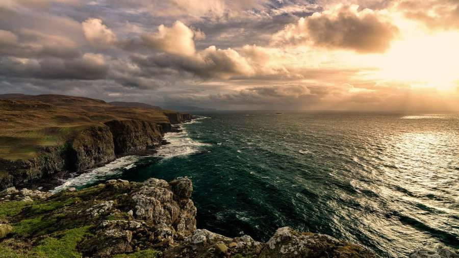 Acantilados escarpados con vistas a olas rompiendo bajo un amanecer dorado con nubes dramáticas. — Línea costera Fondos de pantalla