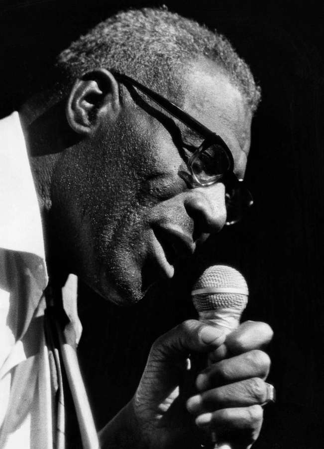 Homem de óculos cantando em um microfone no palco em preto e branco. — Lobo Howlin Papéis de Parede