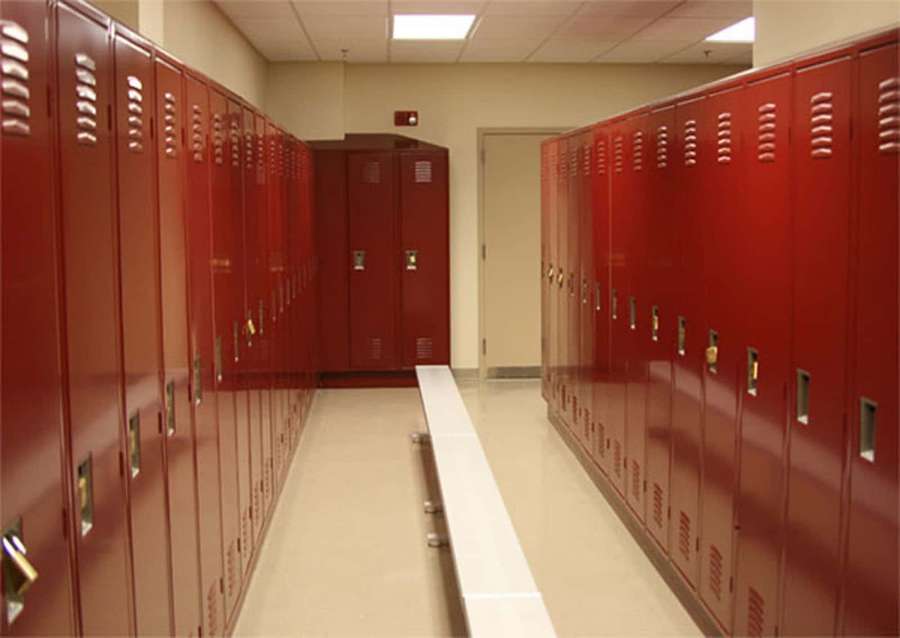 Red school lockers line a quiet hallway with a white bench and fluorescent lighting. — Locker Background