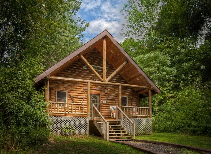 Rustic log cabin with porch surrounded by green trees on a sunny day. — Log Cabin Picture