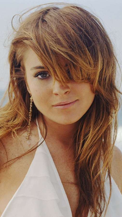 Donna con capelli al vento e maglietta bianca sorride dolcemente all'aperto. — Lohan Sfondi