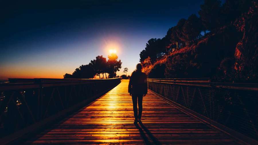 Person walking on wooden bridge at sunset with warm golden light. — Lonely Background