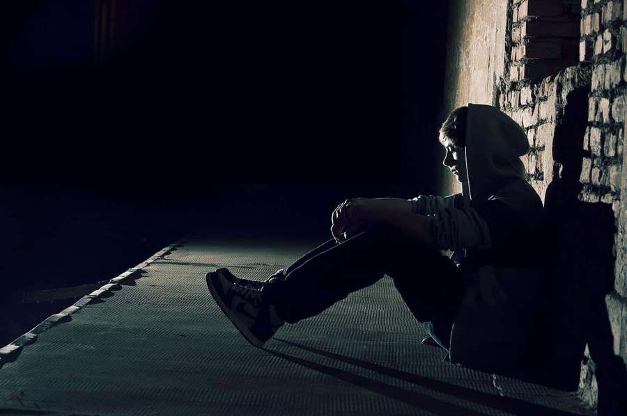 A person in a hoodie sits alone against a brick wall in a dark alley at night. — Loner Wallpaper