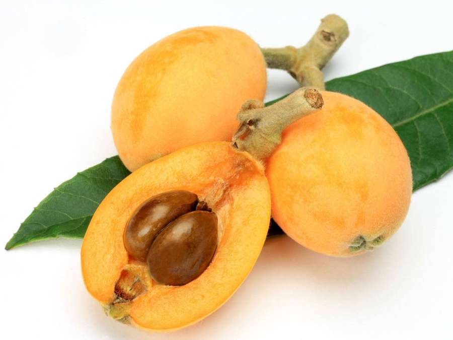 Kolme mispeliä, joista yksi leikattu auki näyttäen siemenet vihreillä lehdillä. — Loquat Taustakuvat