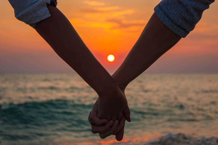 Zwei Menschen, die bei Sonnenuntergang über dem Meer Hände halten. — Love Hand Bilder