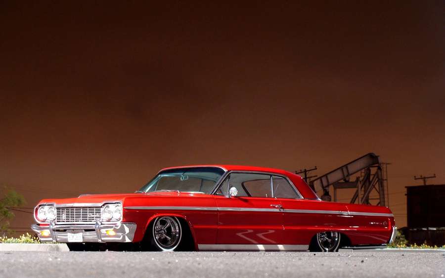 A red classic lowrider car parked on a street at twilight. — Lowrider Background