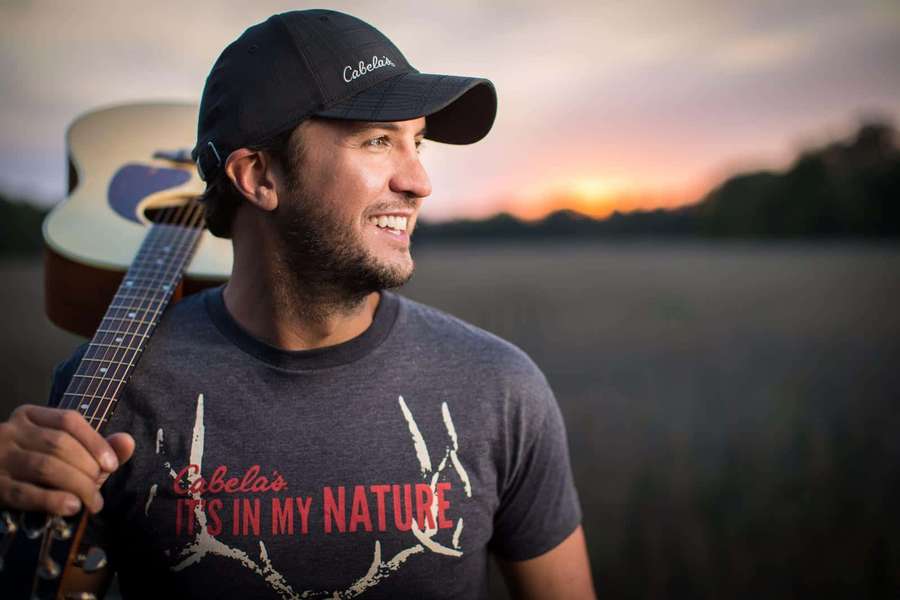 Pria memegang gitar tersenyum saat matahari terbenam di ladang — Luke Bryan Wallpaper