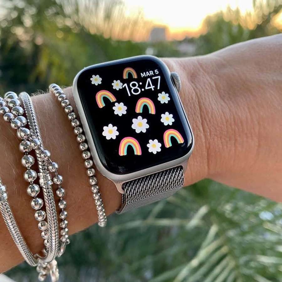 Pulso com pulseiras de prata e smartwatch mostrando papel de parede de arco-íris e margarida ao pôr do sol. — Maçã Papéis de Parede