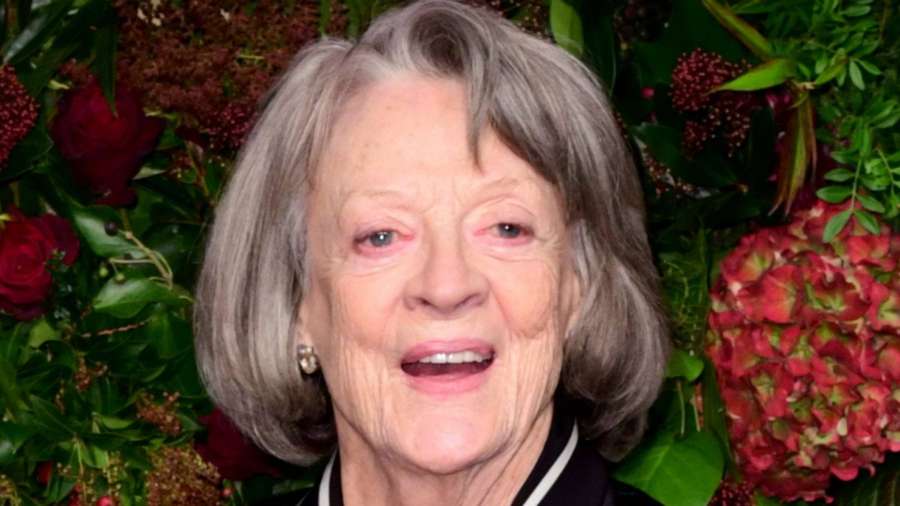 Ältere Frau mit grauem Haar, die vor roten Blumen und grünem Laub lächelt. — Maggie smith Wallpaper