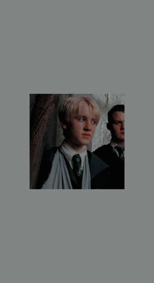 Young man with blonde hair in school uniform standing near stone wall. — Malfoy Wallpaper