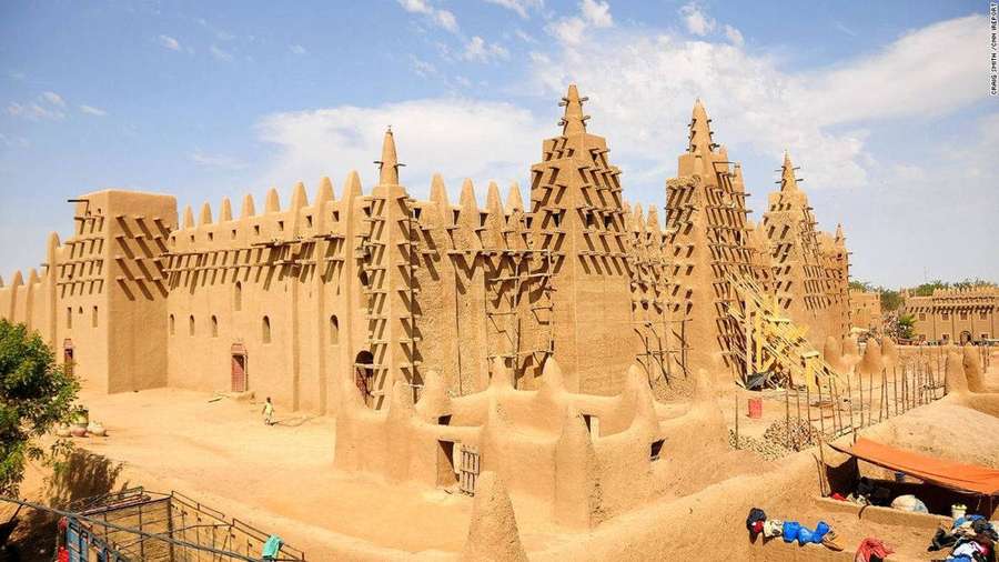 A large historic mud mosque with tall towers under a blue sky with clouds. — Mali Wallpaper