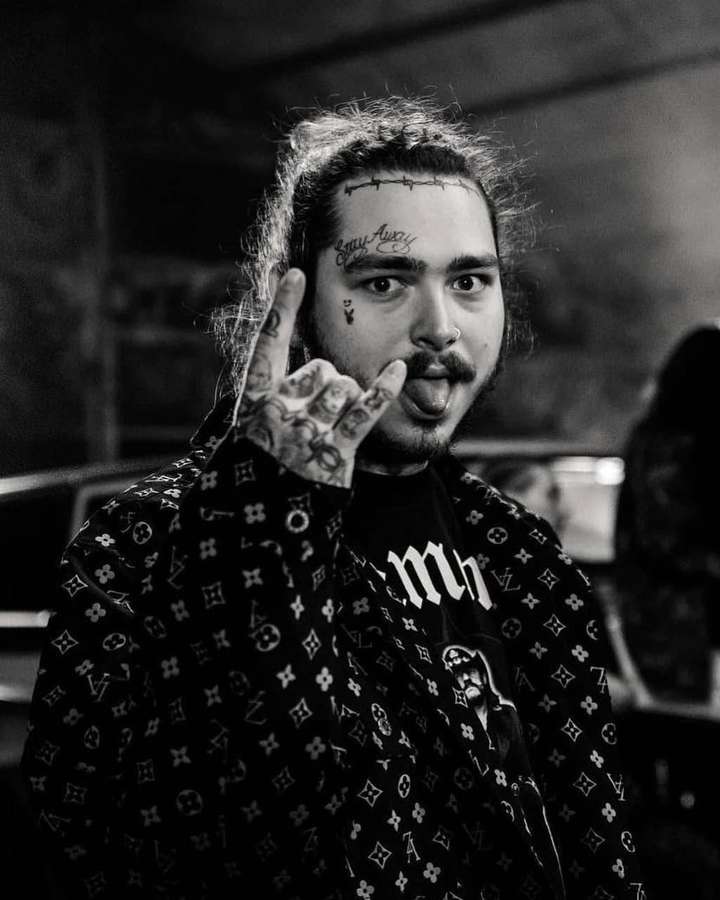 A tattooed man in a patterned jacket making a hand gesture and sticking out his tongue. — Malone Background