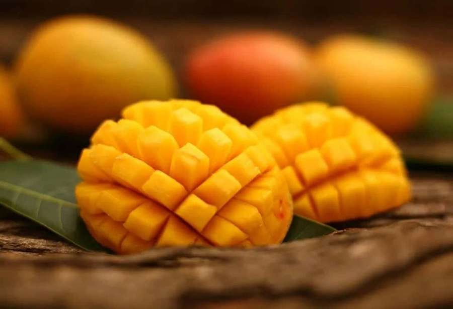 Two diced mangoes on leaves with whole mangoes blurred in background. — Mango Picture
