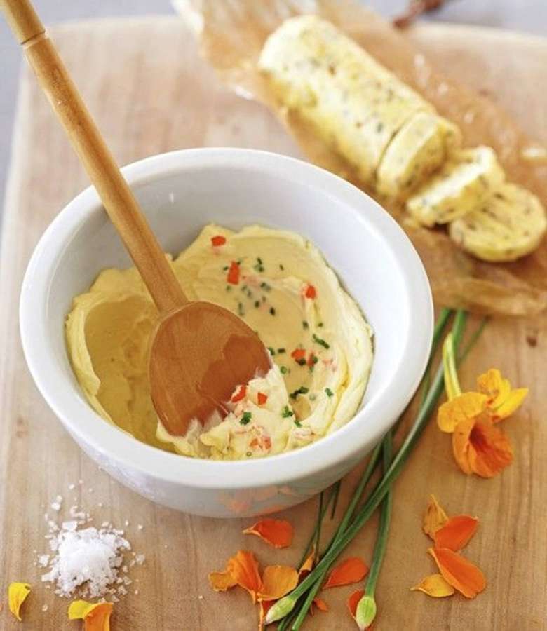 Mantequilla de hierbas cremosa en bol blanco con cuchara de madera y flores frescas sobre tabla de madera. — Mantequilla Fondos de pantalla