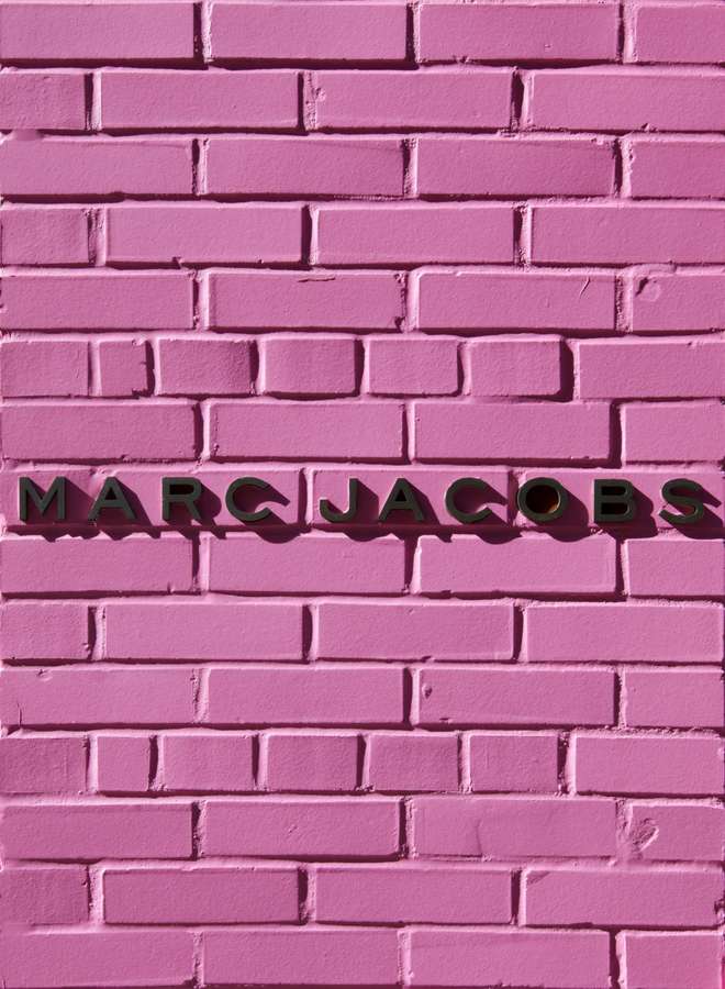 Pink brick wall with black MARC JACOBS signage. — Marc Jacobs Wallpaper