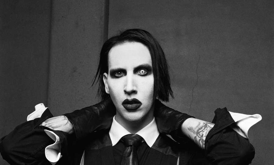 Person with dark makeup and tattoos pulling at shirt collar in black and white. — Marilyn manson Wallpaper