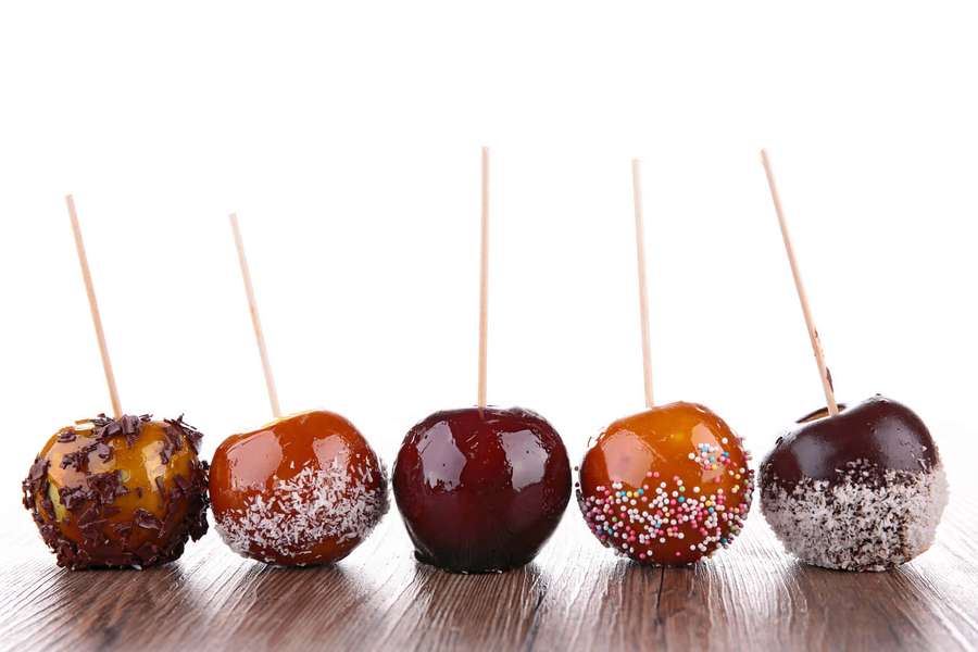 Cinco manzanas acarameladas decoradas en palitos dispuestas sobre una superficie de madera. — Marrón Caramelo Fondos de pantalla