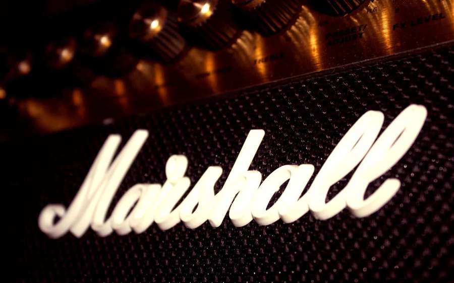 Marshall amplifier logo with glowing white script on black grille and golden knobs. — Marshall Background