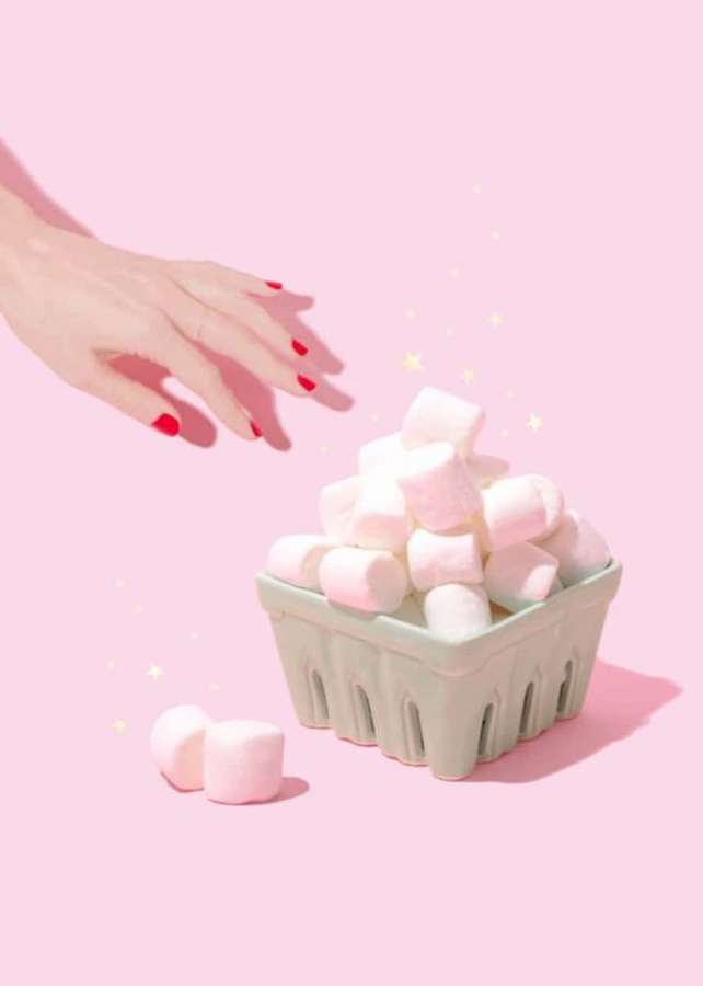 Hand mit roten Nägeln, die nach rosa Marshmallows in einem Korb auf rosa Hintergrund mit Glitzern greift — Marshmallow Bilder