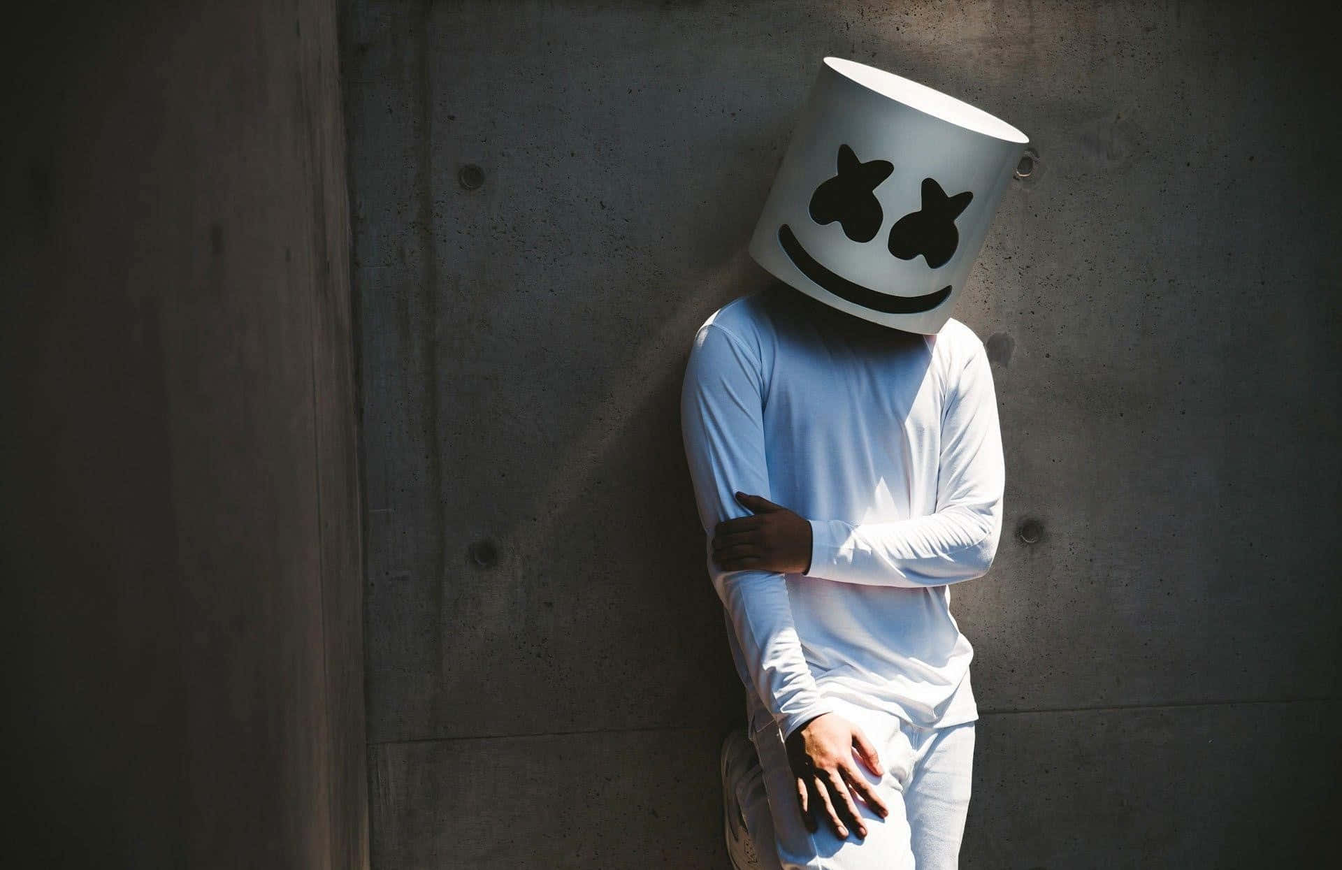 Person som bär en vit bucket hat med smiley-ansikte lutar sig mot betongvägg. — Marshmello bakgrund Bakgrundsbilder