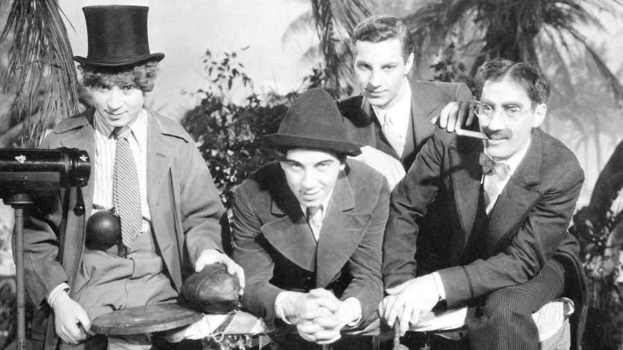 Four vintage-dressed men posing with camera and props in palm tree setting. — Marx Brothers Wallpaper