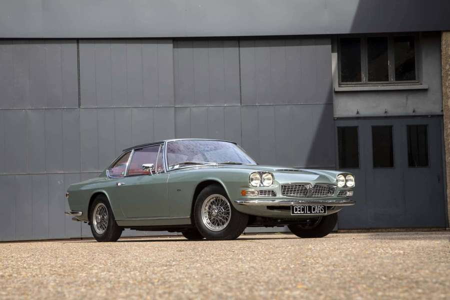 Carro esportivo verde sálvia vintage estacionado em cascalho perto de edifício industrial cinza. — Maserati Mexico Papéis de Parede