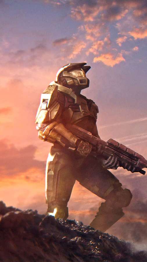 Spartan soldier in futuristic armor holding a weapon on a rocky hill at sunset. — Master Chief Phone Wallpaper
