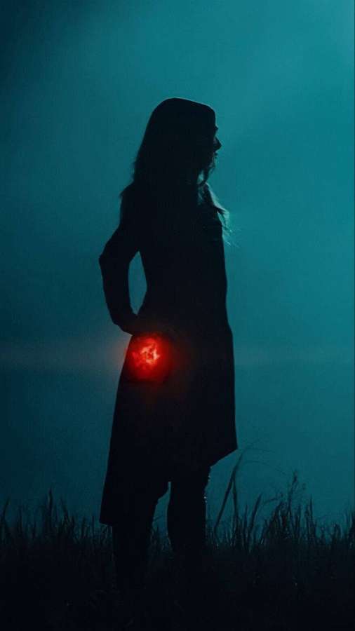 A hooded figure stands in fog holding a glowing red orb in a teal-lit night scene. — Maximoff Wallpaper