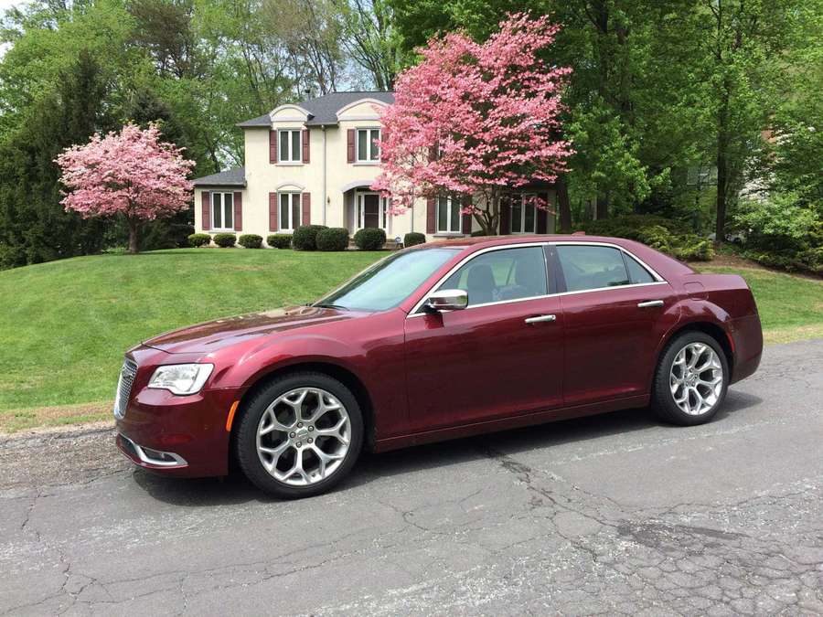 Maroon sedan parked in front of a house with pink flowering trees. — Mazda 323 Wallpaper