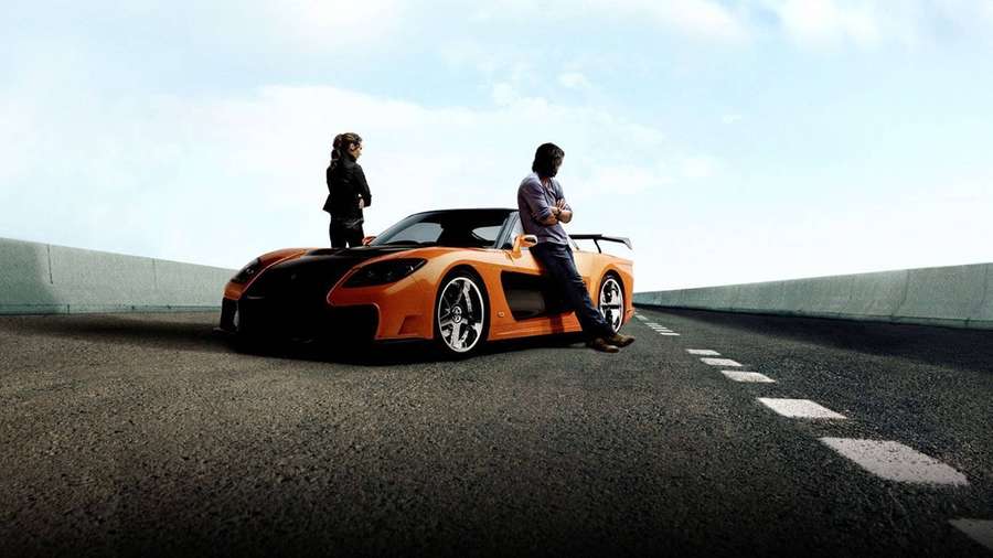 Zwei Personen neben einem orangefarbenen Sportwagen auf einer Autobahn bei Sonnenuntergang. — Mazda Rx 7 Hintergrundbild