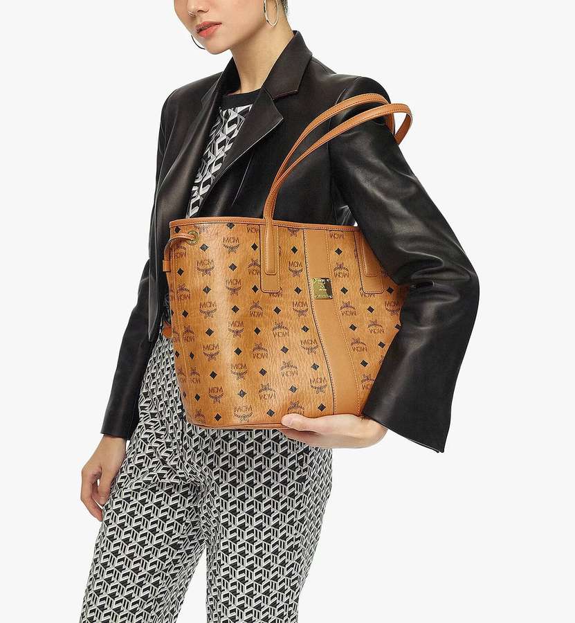 Woman holding a tan logo-printed bucket bag with black leather jacket and geometric pants. — Mcm Wallpaper